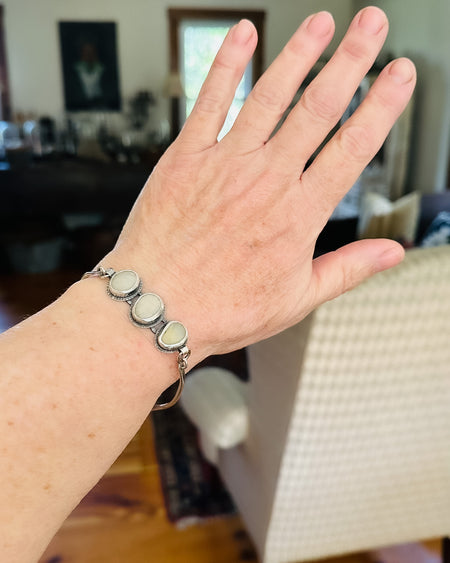 Hand wearing a silver bracelet with three white beach stones
