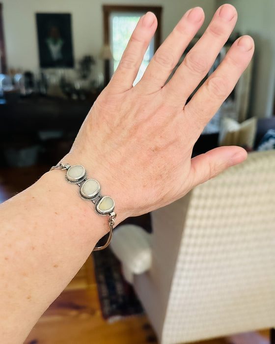 Hand wearing a silver bracelet with three white beach stones
