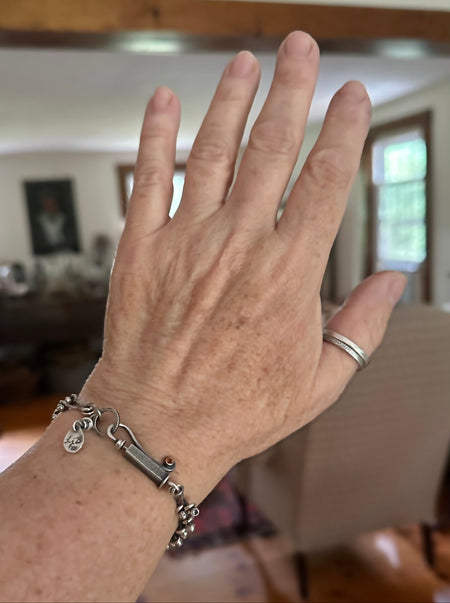A close-up of a person's hand wearing a silver chain bracelet , with a blurred indoor home background.