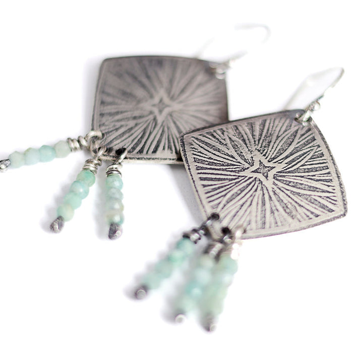 Silver earrings with starburst design and aquamarine beads on a white background