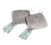 Silver earrings with starburst design and aquamarine beads on a white background