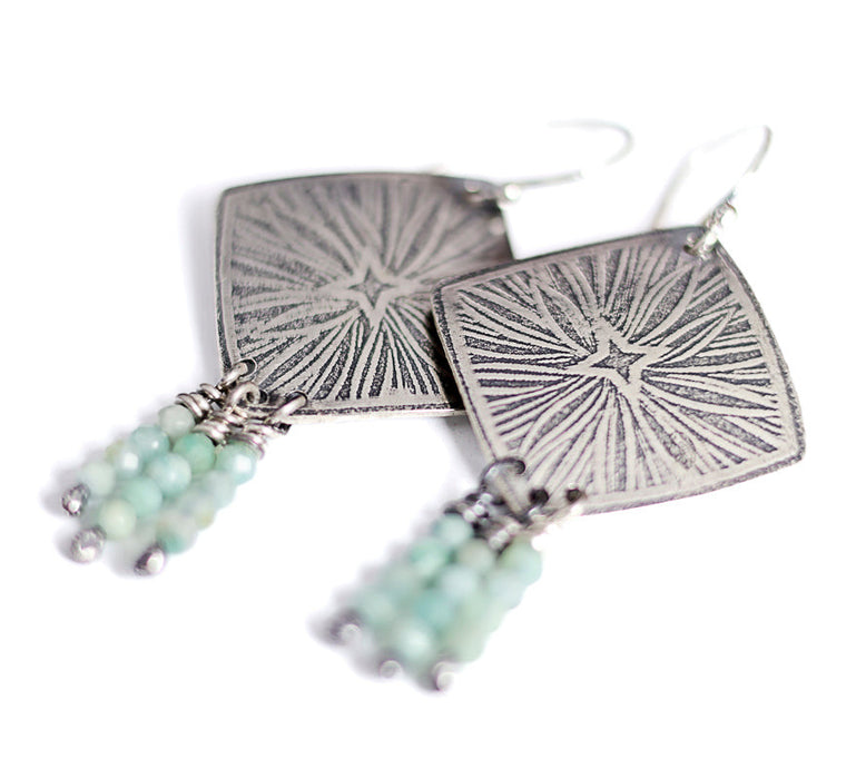 Silver earrings with starburst design and aquamarine beads on a white background