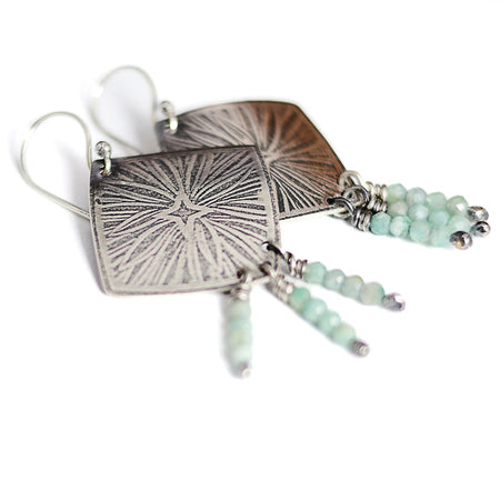 Silver earrings with starburst design and aquamarine beads on a white background