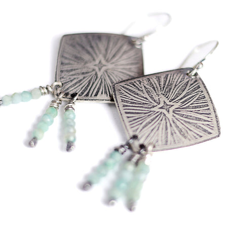 Silver earrings with starburst design and aquamarine beads on a white background