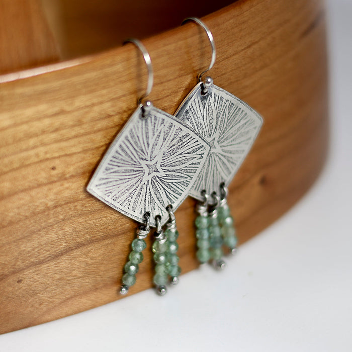 Silver earrings with green apatite beads on a wooden surface