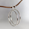 Silver hoop earrings on a thin brown cord against a light gray background