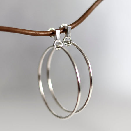Silver hoop earrings on a thin brown cord against a light gray background