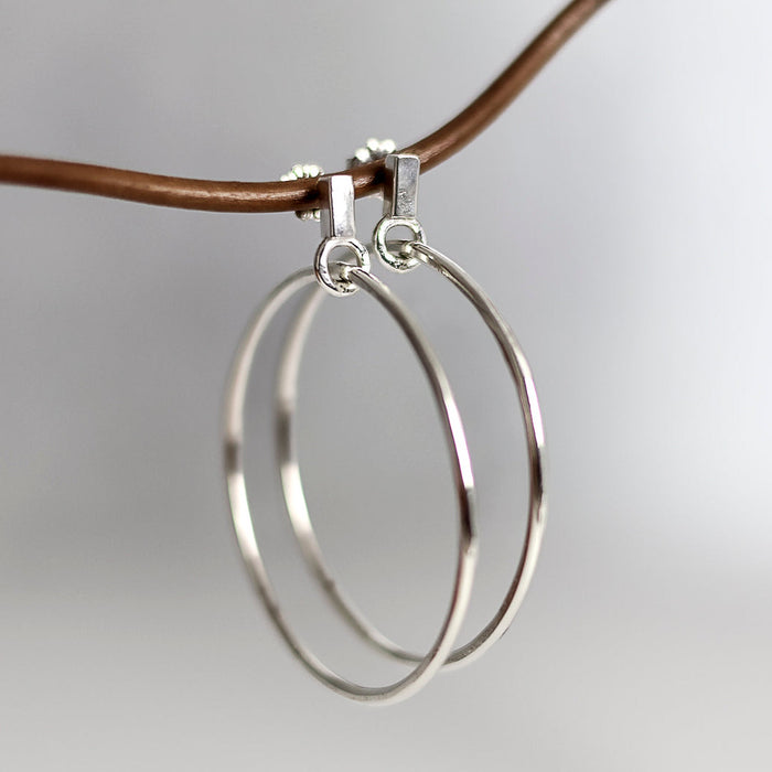 Silver hoop earrings on a thin brown cord against a light gray background