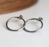 Silver hoop earrings on a white surface with a wooden background