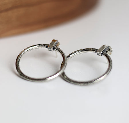 Silver hoop earrings on a white surface with a wooden background