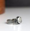 Silver ring with a textured band and round stone on a white surface