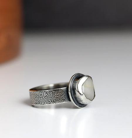 Silver ring with a textured band and round stone on a white surface