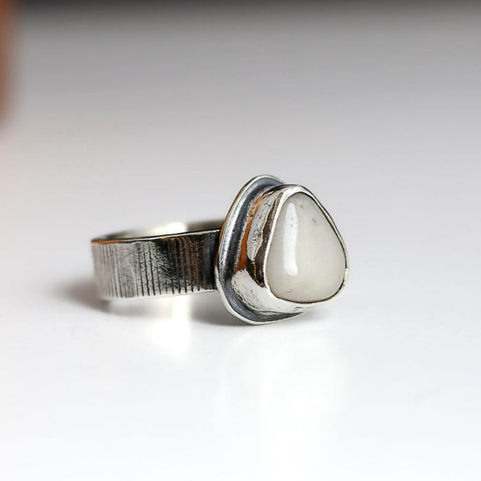 Silver ring with a white stone on a light gray background