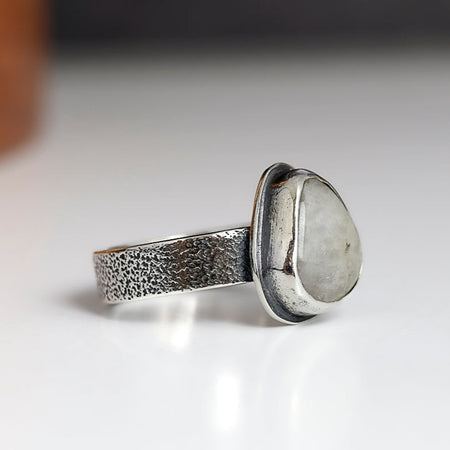 Silver ring with a textured band and smooth stone on a white background