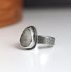 Silver ring with a textured band and pebble-shaped stone on a white background