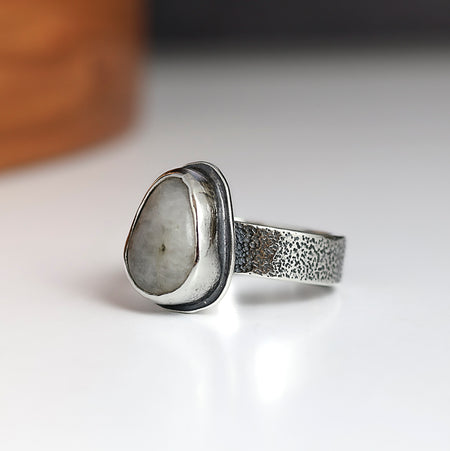 Silver ring with a textured band and pebble-shaped stone on a white background