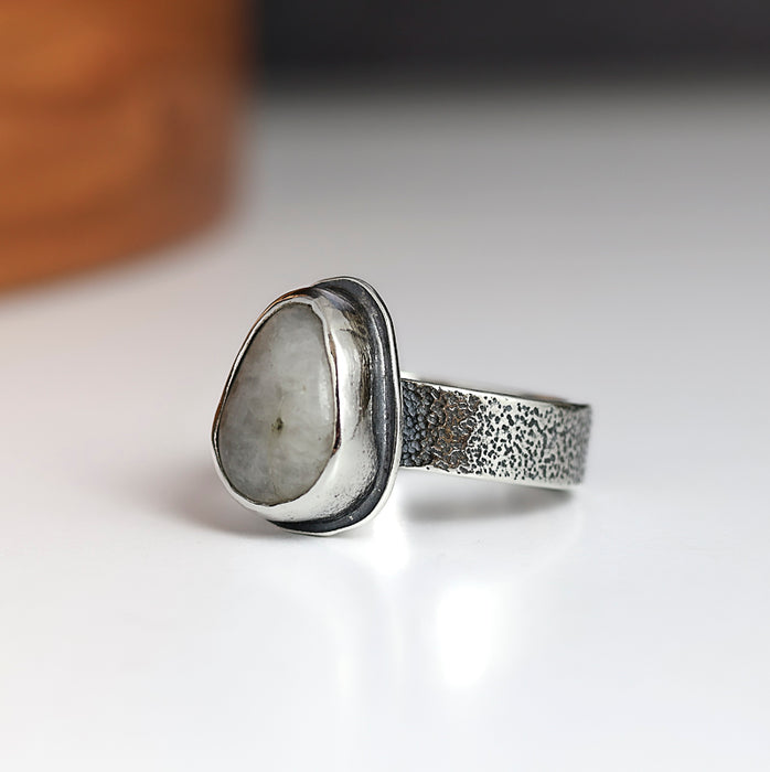 Silver ring with a textured band and pebble-shaped stone on a white background