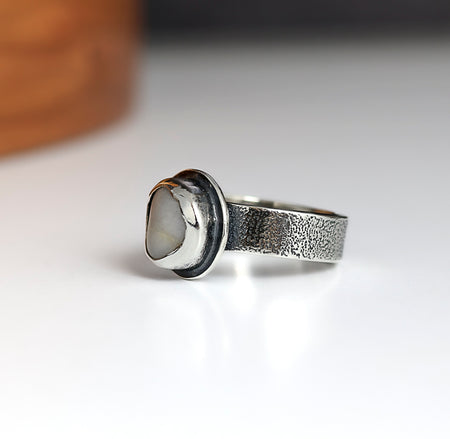 Silver ring with a textured band and stone on a white background