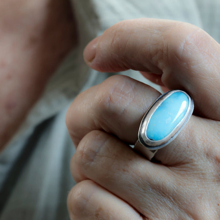 A close-up of a hand wearing a silver ring with a smooth, oval light blue turquoise cabochon gemstone.
