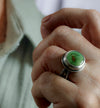 A close-up of a hand wearing a silver ring with a round green turquoise stone