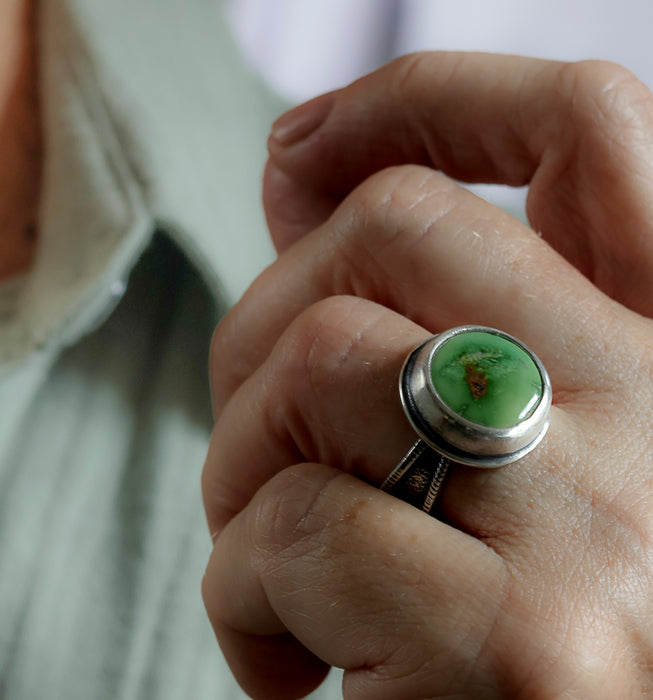 A close-up of a hand wearing a silver ring with a round green turquoise stone