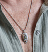 Close-up of a person wearing a silver necklace with a detailed pendant.
