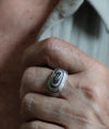 Close-up of a hand wearing a silver ring with a multicolored stone.
