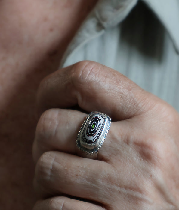 Close-up of a hand wearing a silver ring with a multicolored stone.