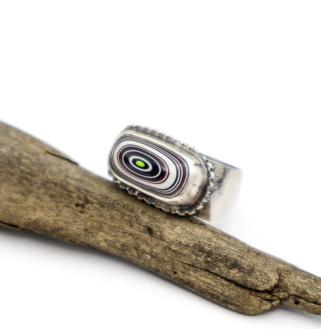 Silver ring with a multicolored stone on a wooden branch