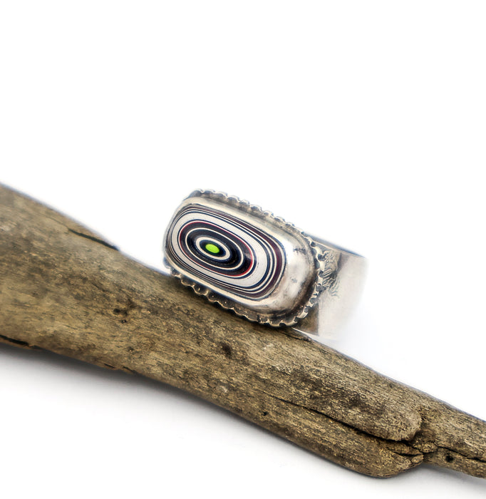 Silver ring with a multicolored stone on a wooden branch
