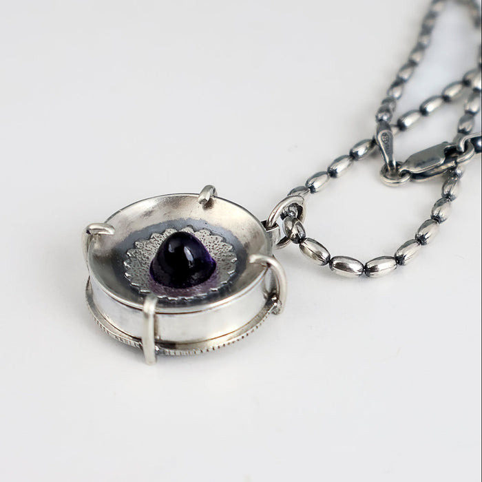 Handmade sterling silver pendant with high dome amethyst in a sand textured flower frame inside a pronged silver cup, on an oval bead chain