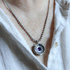 Handmade sterling silver pendant worn by a person with high dome amethyst in a sand textured flower frame inside a pronged silver cup, on an oval bead chain
