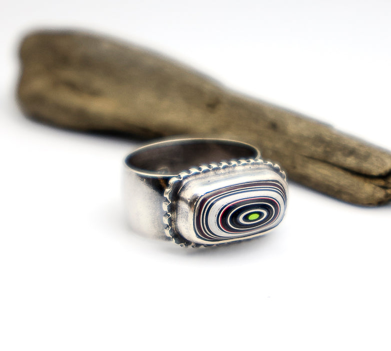Silver ring with a multicolored stone on a white background