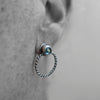 Close-up of an ear wearing a silver hoop earring with a gemstone.