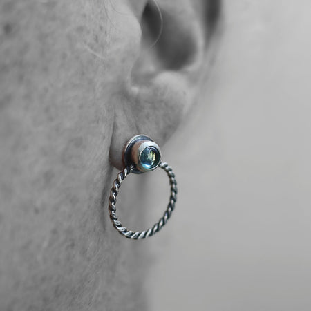 Close-up of an ear wearing a silver hoop earring with a gemstone.