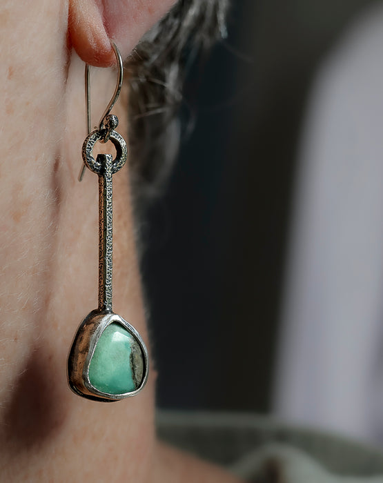 Sterling silver dangle earrings worn on a ear with green turquoise stones and hand textured square wire, handmade by LjB Jewelry, 