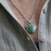 Necklace with a heart-shaped green turquoise pendant worn by a person in a light-colored shirt.