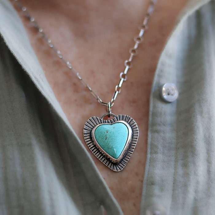 Necklace with a heart-shaped turquoise pendant worn by a person in a light-colored shirt.