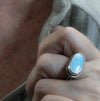A close-up of a hand wearing a silver ring with an oval turquoise  stone.
