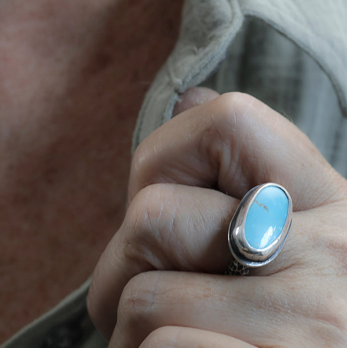 A close-up of a hand wearing a silver ring with an oval turquoise  stone.
