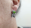 Silver earring with a green gemstone worn on an ear against a neutral background