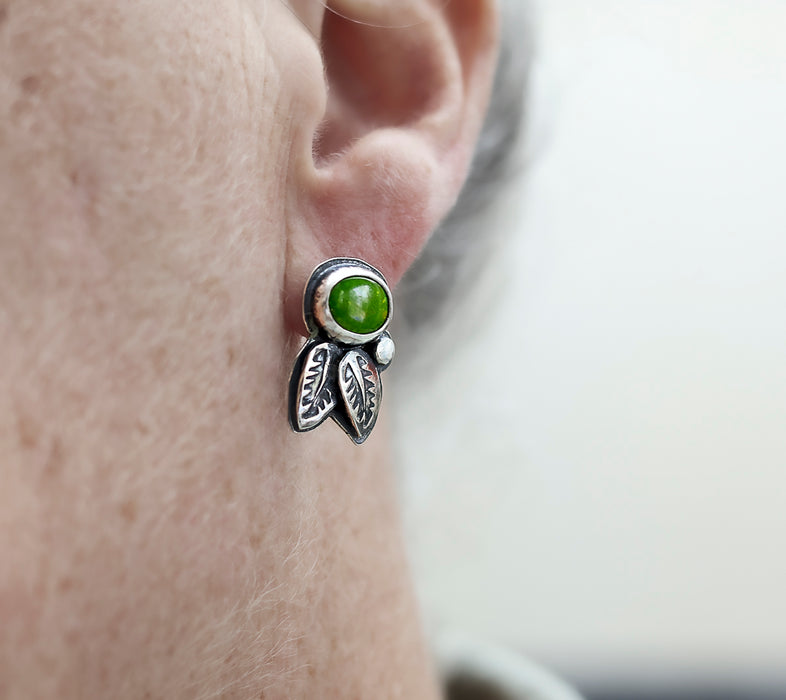 Silver earring with a green gemstone worn on an ear against a neutral background