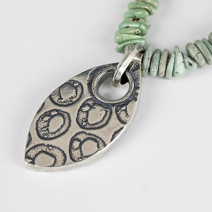 Necklace with a silver pendant and turquoise beads on a light gray background