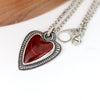 Heart-shaped pendant with red stone on a silver chain against a white background