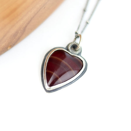 Heart-shaped red stone pendant on a silver chain against a white background