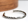 Silver twisted cuff bracelet on a white surface with a wooden object in the background
