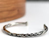 Silver twisted cuff bracelet on a white surface with a wooden object in the background
