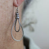 Silver twisted rope earring on a person's ear with a blurred background