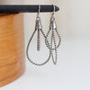 Silver rope-style earrings on a wooden stand with a white background