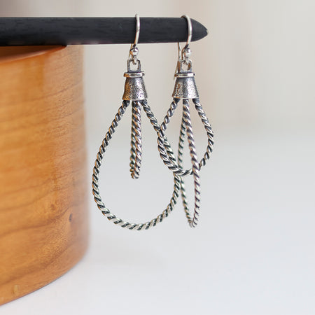 Silver rope-style earrings on a wooden stand with a white background
